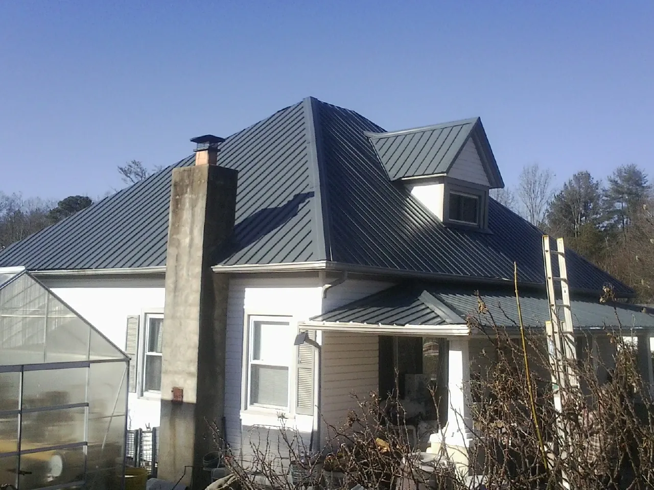 Dark blue standing seam metal roof on a white farmhouse with dormer — Slate & Tile Roof Repair by Roofing Brothers in Albia