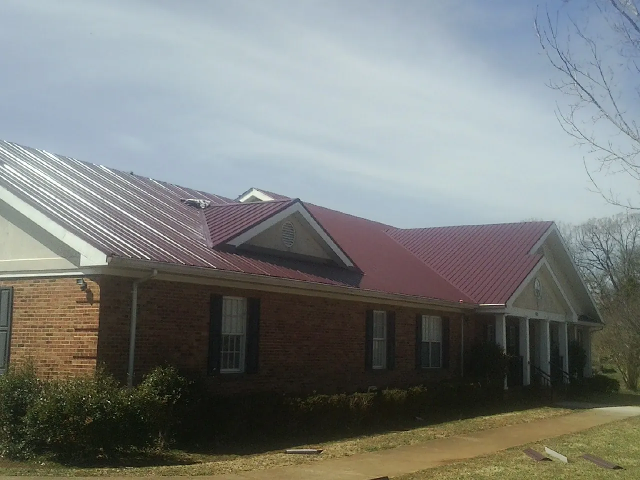 Red metal roof with gabled entries on a long brick building, from a Hail Damage Roof Repair job in Albia