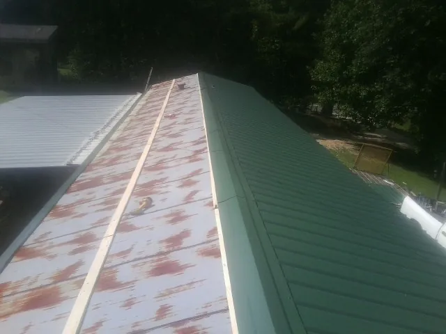 Old rusted panels beside newly installed green metal roofing — Wind Damage Roof Repair by Roofing Brothers in Albia