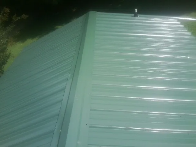 New green metal panels meeting at the ridge of a roof — Flat Roof Repair work by our crew in Albia