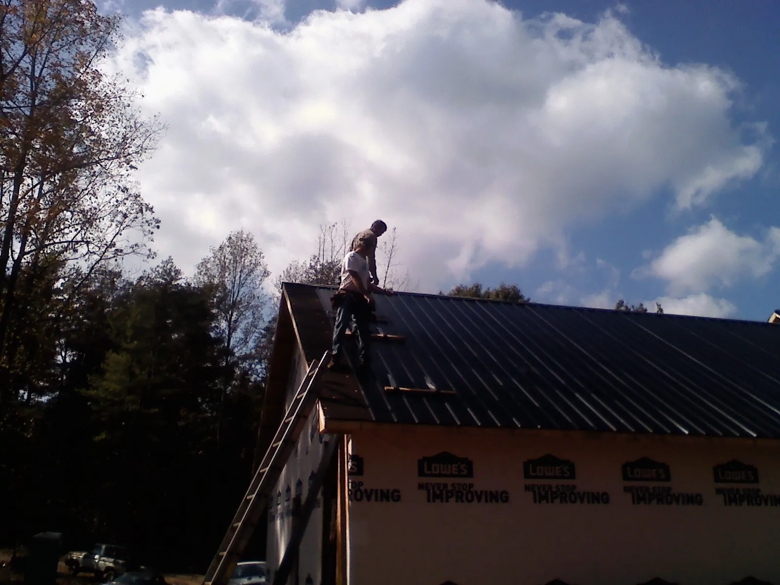 Roofer fastening dark metal panels high against a cloudy sky, from a Roof Inspection job in Albia