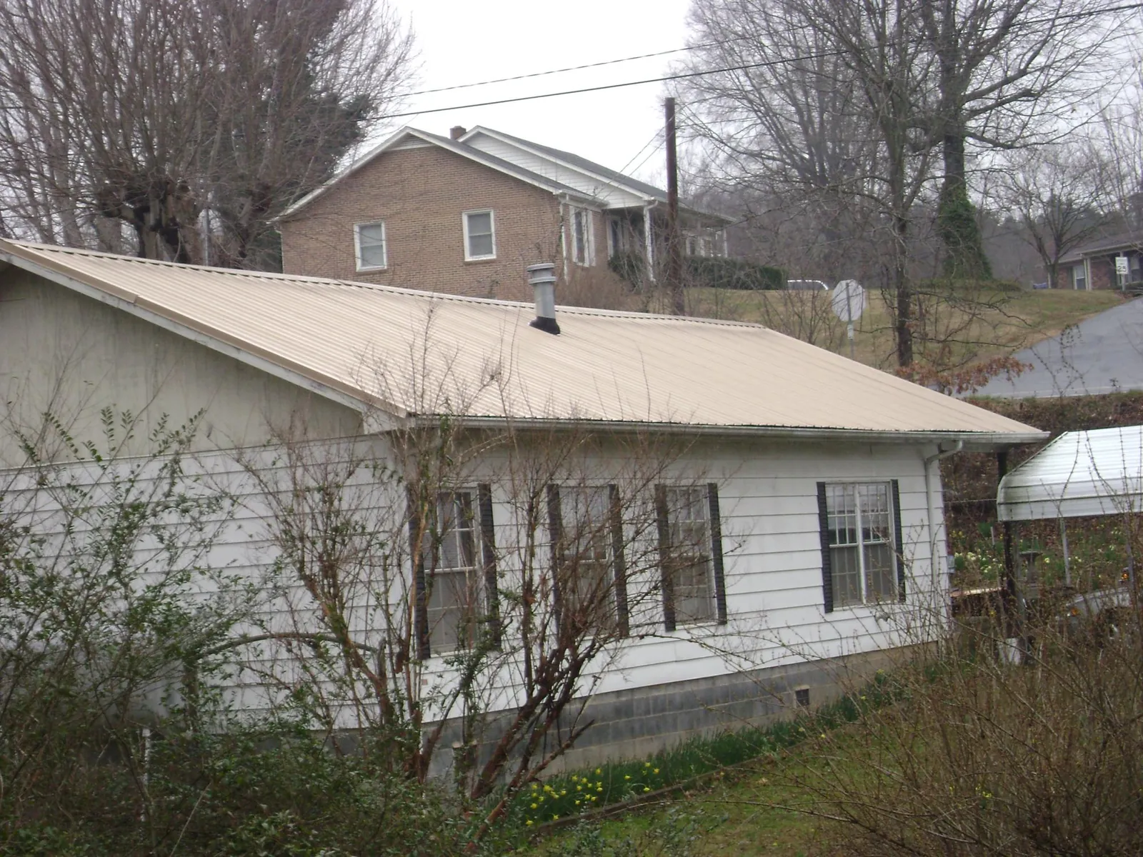 Tan metal roof on a white sided house set into a hillside — Commercial Roofing by Roofing Brothers in Albia
